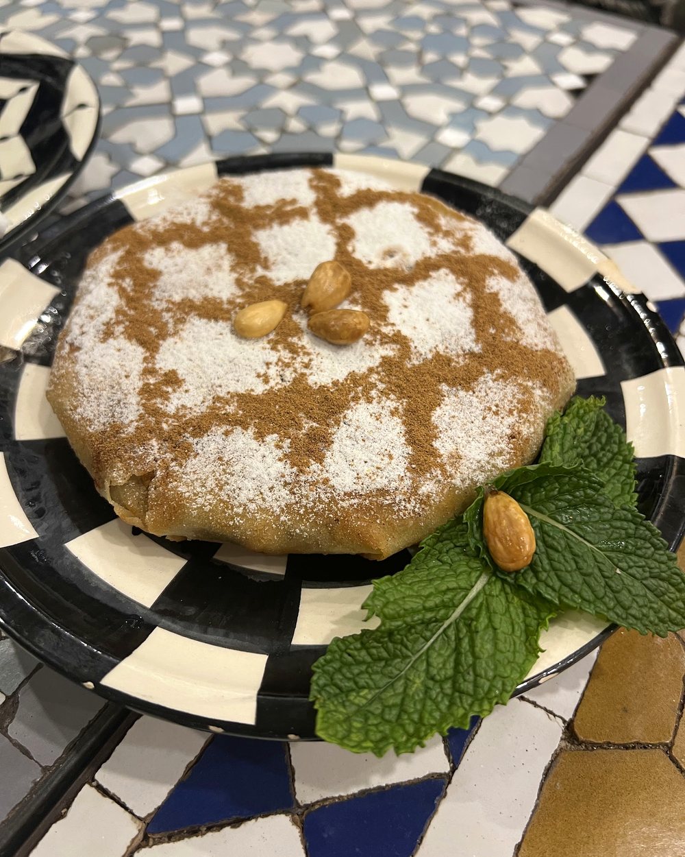 Pastilla dorée au sucre glace et amandes, servie sur céramique marocaine